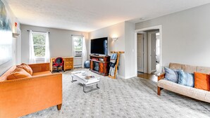 Un salon avec un canapé, une table basse et un meuble pour la télévision. Une porte donne accès à une autre pièce.
