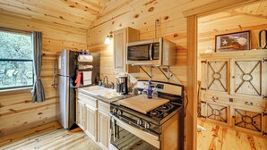 A wooden cabin kitchen with a refrigerator, stove, microwave, and wooden cabinets. - Cozy Cabin Hill Country Escape w/ Views (Johnson City)