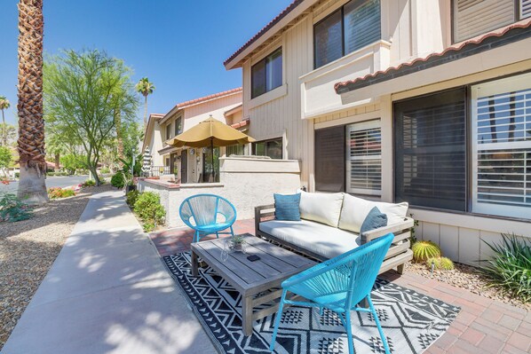 A patio with a wooden table, two blue chairs, a white sofa, and a patterned rug.