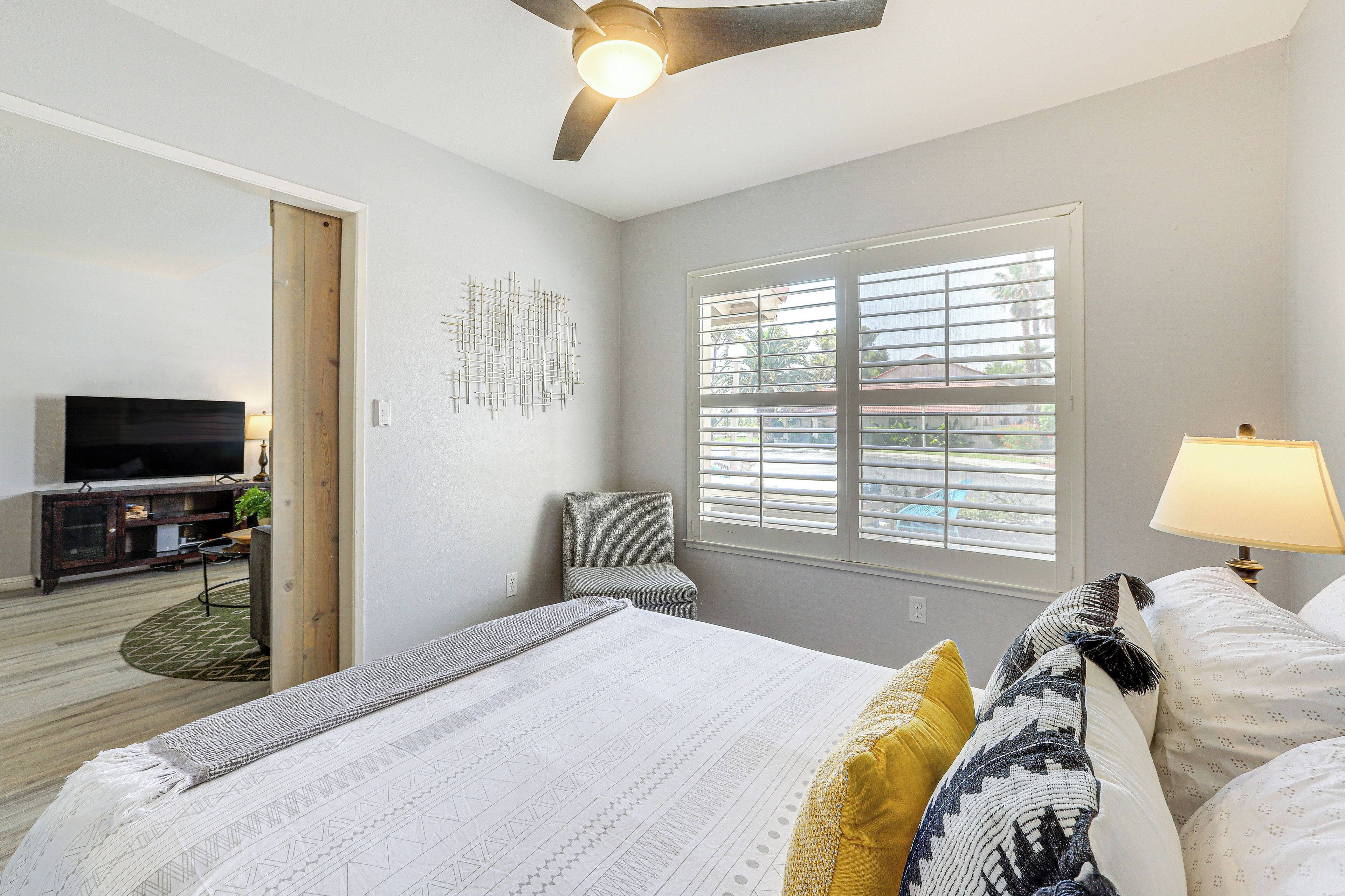 A bedroom with a bed, a chair, a TV, and a window with blinds.