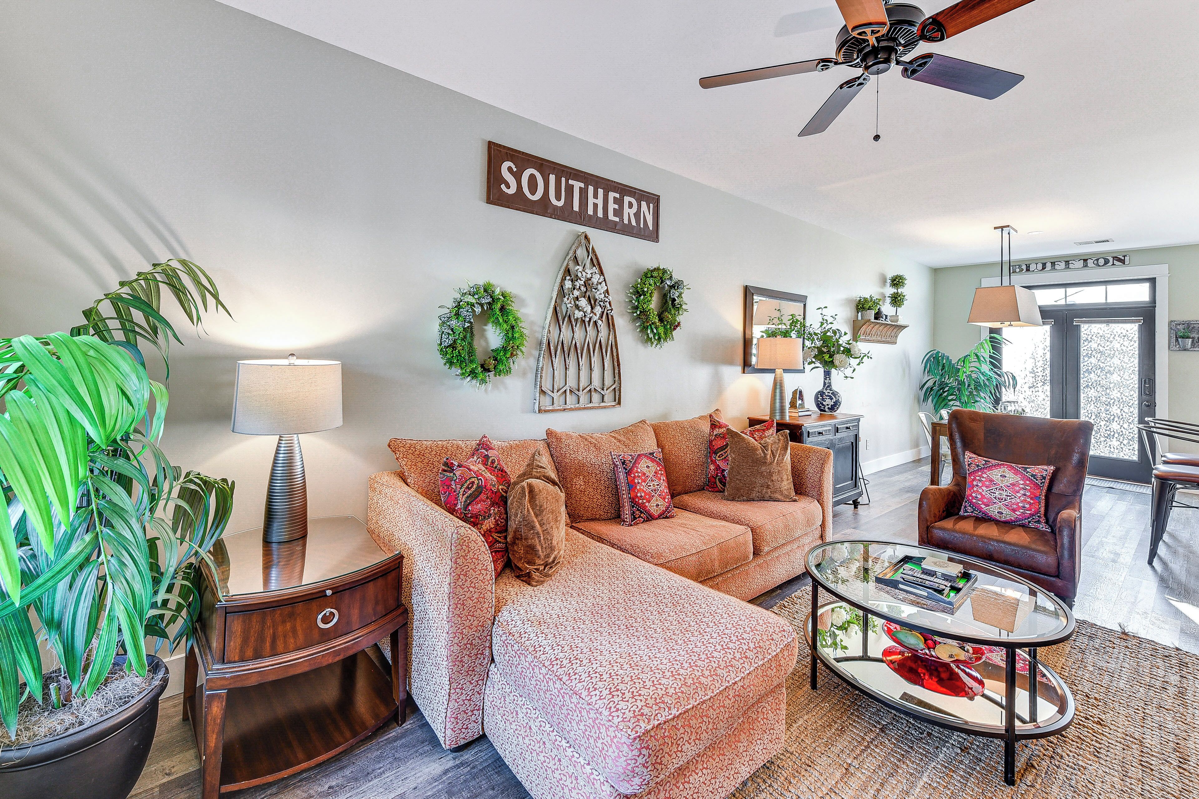 A living room with a sectional sofa, a glass coffee table, a side table, and a potted plant.