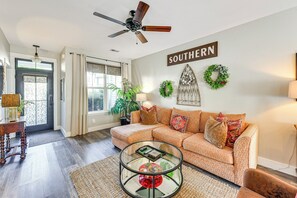 A living room with a sofa, a glass coffee table, and a ceiling fan.
