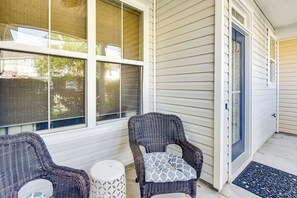 A porch with two wicker chairs and a small table, a blue door, and a window with a view of trees.