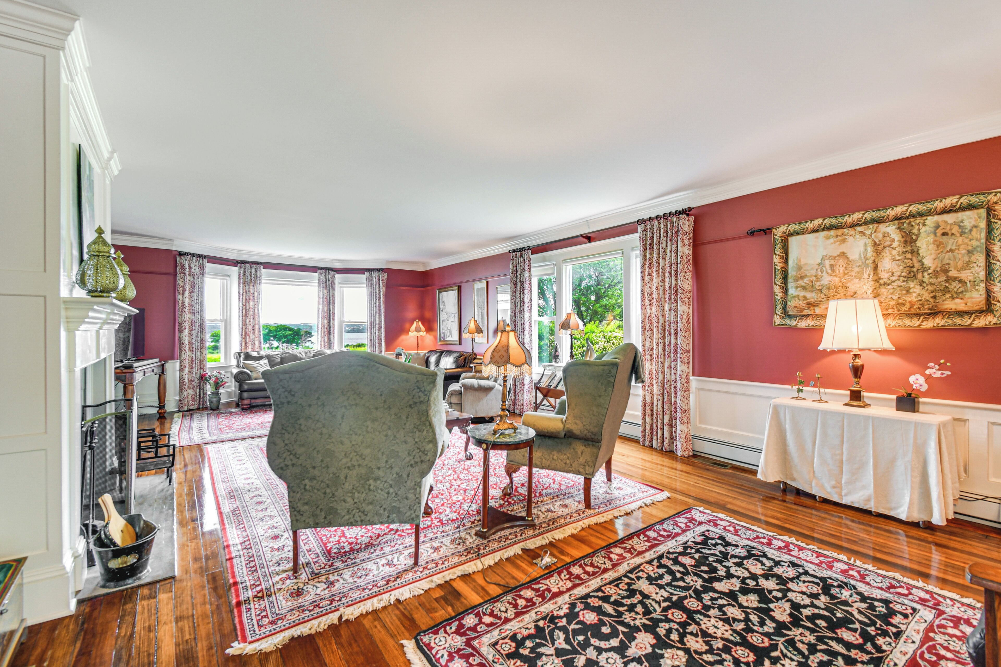 A spacious living room with a fireplace, two armchairs, a coffee table, and a large window with curtains.