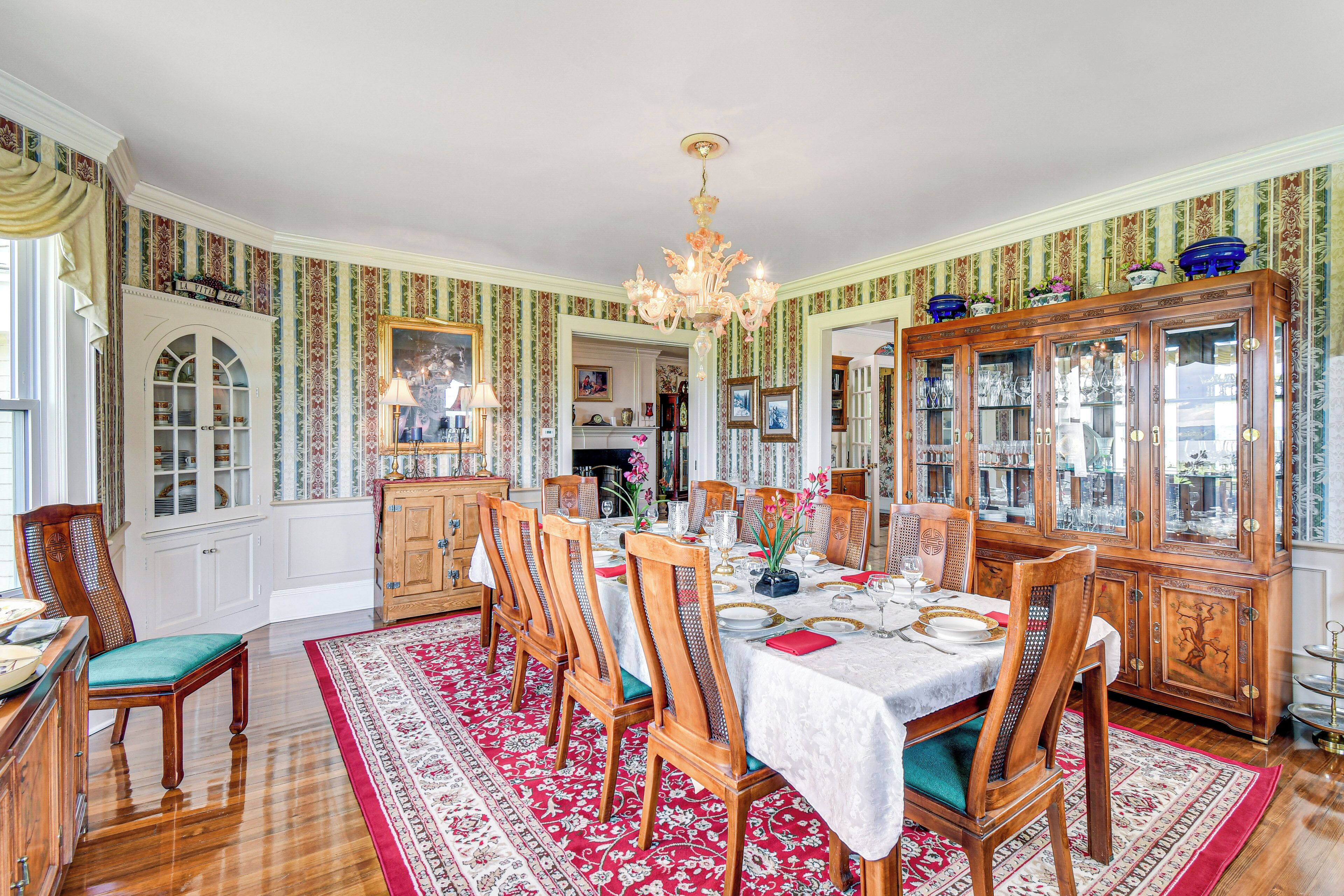A dining room with a large wooden table, chairs, and a red patterned rug.