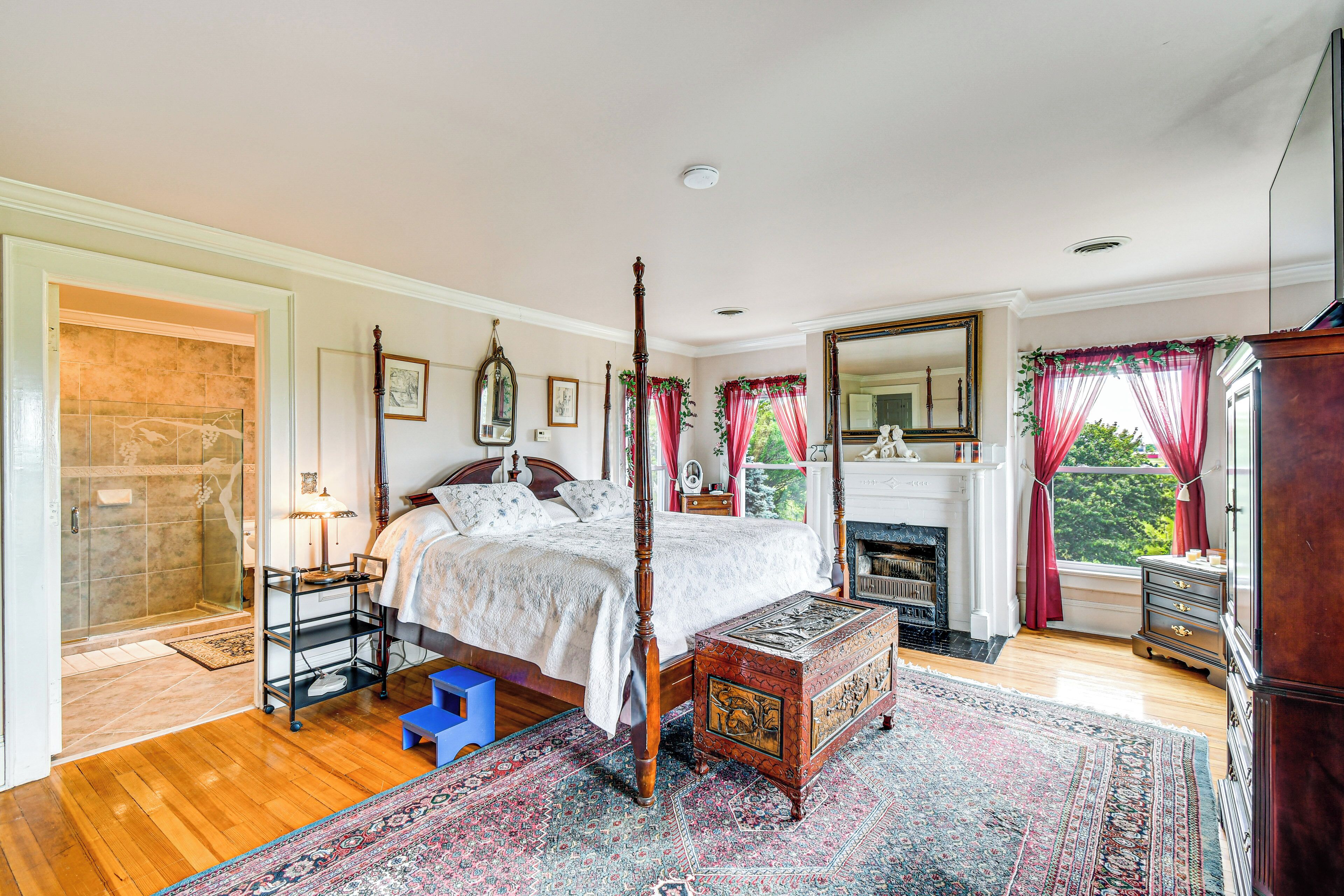 A spacious bedroom with a large bed, a four-poster, a fireplace, and a view of greenery outside.
