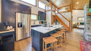 A spacious kitchen with a large island, wooden bar stools, and a stainless steel refrigerator. - Tree-lined Broken Bow Studio Cabin w/ Hot Tub! (Broken Bow)
