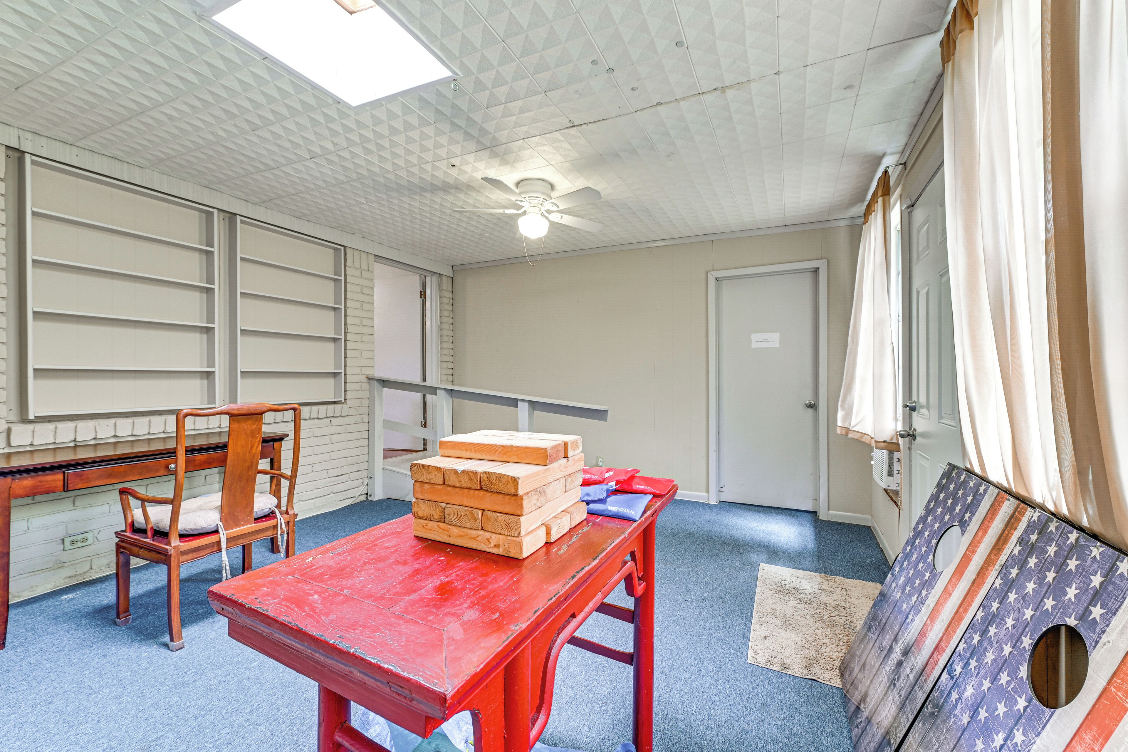 Une pièce avec une table rouge, une chaise en bois, un ventilateur de plafond et une porte avec des rideaux.