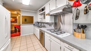 A modern kitchen with white cabinets, stainless steel appliances, and a red hanging pot rack. - Large Yard & Fire Pit! Home 13 Mi to At&t Stadium (Fort Worth)