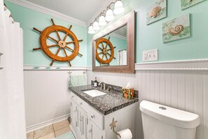 Een badkamer met een wastafel, spiegel en toilet. Er zijn decoratieve schelpen aan de muur en een roerpropeller boven de spiegel.