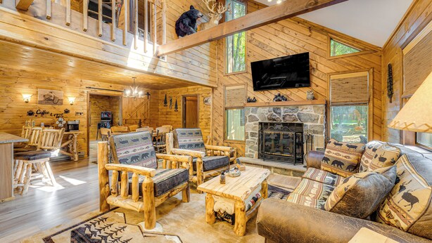 A log cabin interior with a fireplace, wooden furniture, and a mounted bear head.