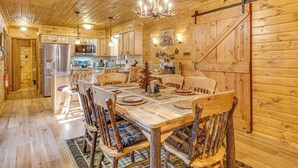 A rustic wooden interior with a dining table set for four, surrounded by wooden chairs with blue cushions.