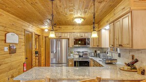 A wooden cabin interior with a kitchen featuring granite countertops, stainless steel appliances, and wooden cabinets.