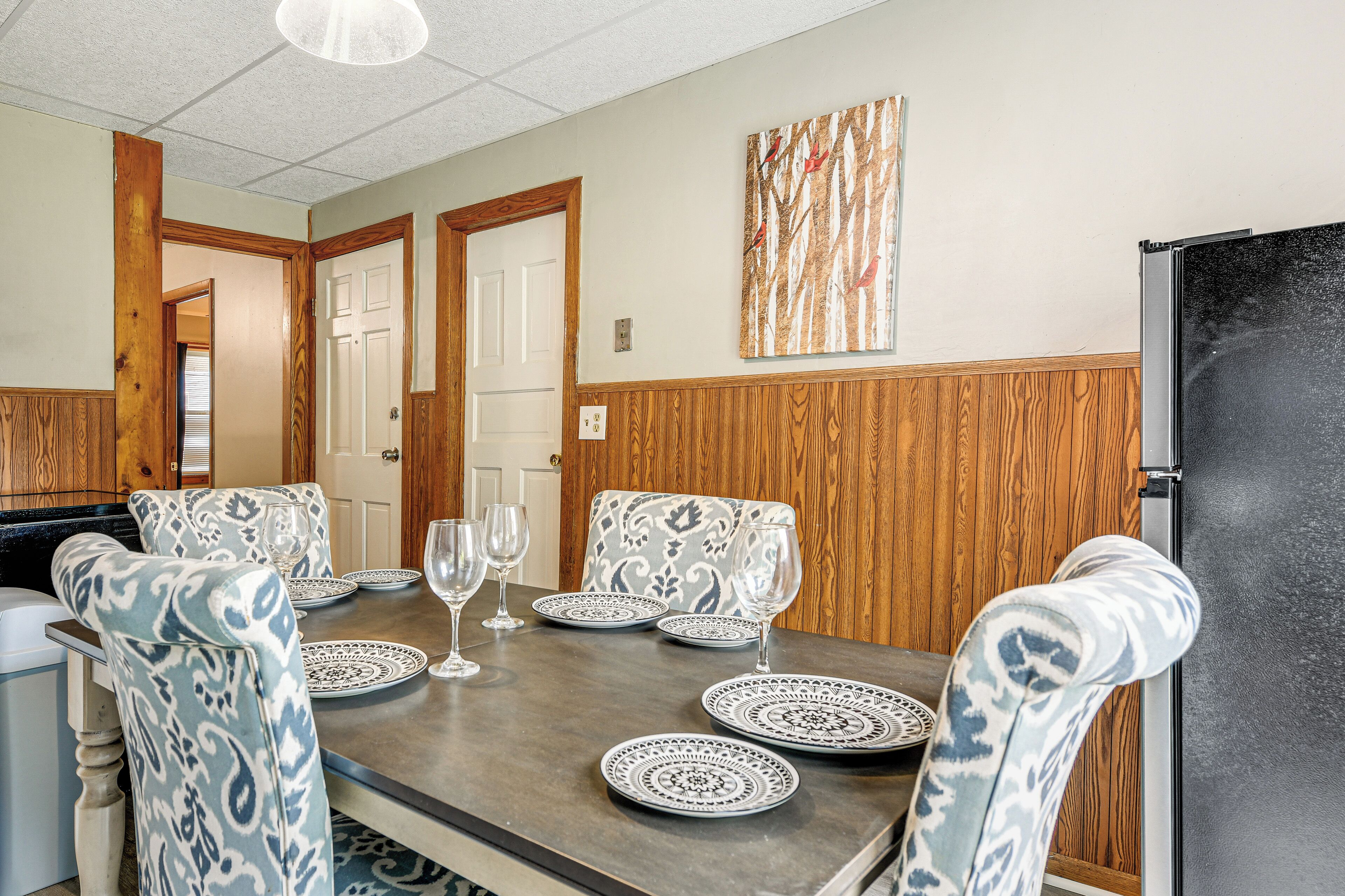 A dining area with a wooden table, patterned chairs, and a black refrigerator.