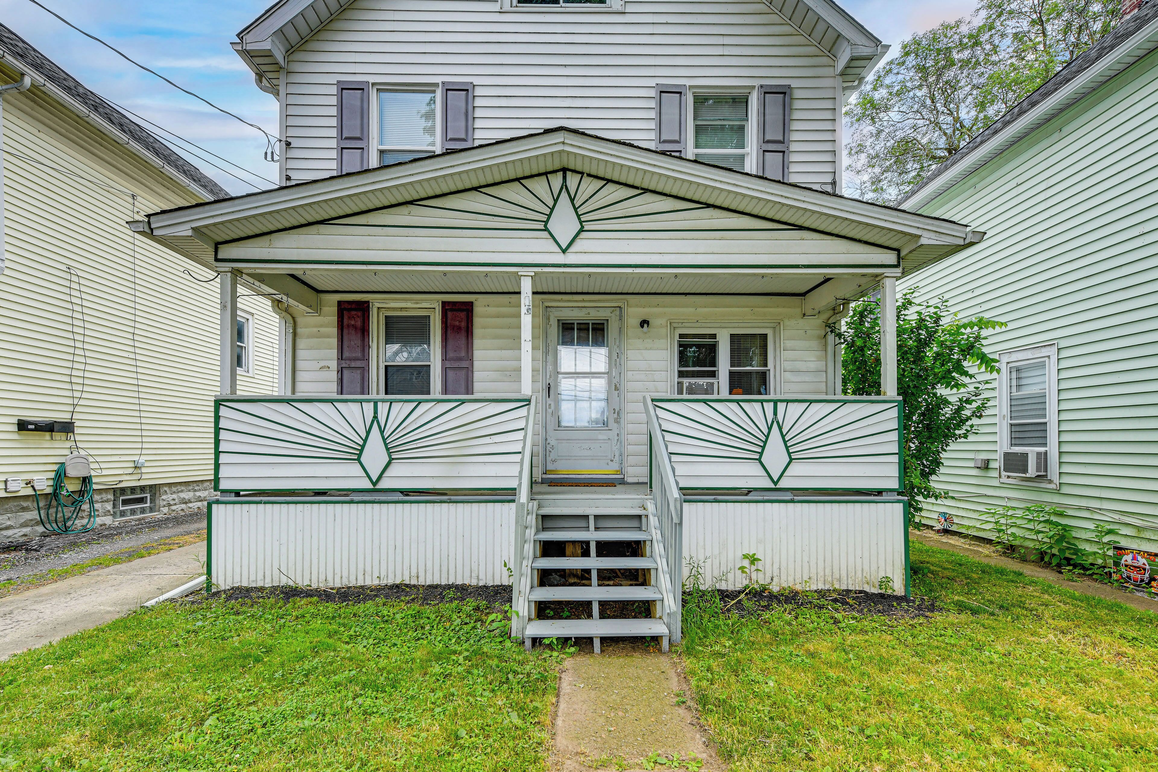 A two-story house with a front porch, a set of stairs leading to the entrance, and a small garden area.