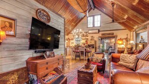Un vaste salon doté d’un grand plafond en bois, d’un canapé en cuir, d’un téléviseur et d’un coin repas agrémenté d’un lustre.