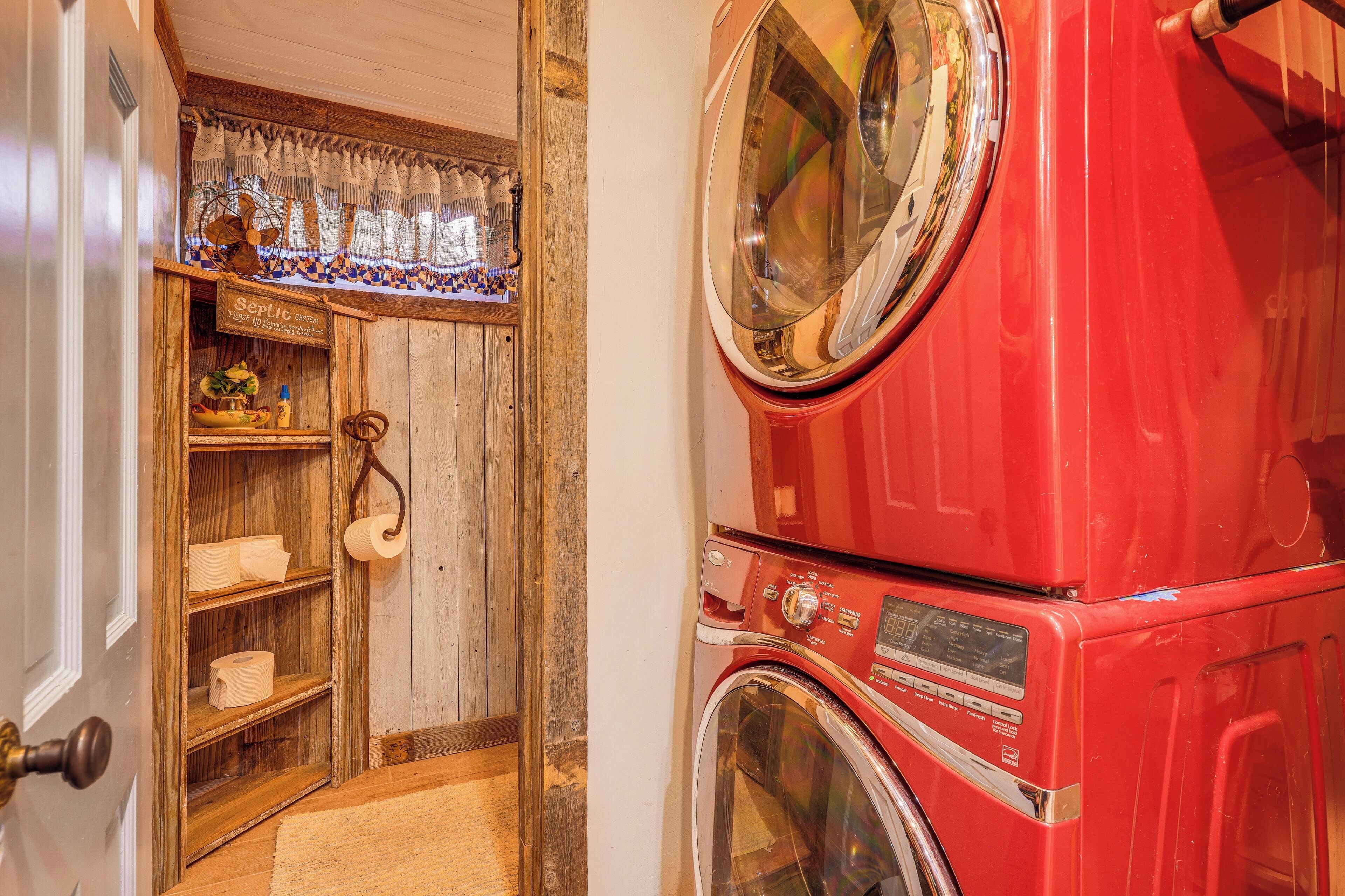 A compact laundry room with a red washing machine and dryer, wooden shelves with towels, and a vintage fan.