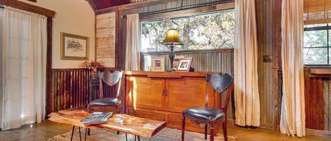 A rustic room with a wooden bench, two leather chairs, a wooden cabinet, and a window with curtains.