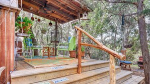 Une terrasse en bois avec des marches menant à une zone abritée, le tout entouré d’arbres.