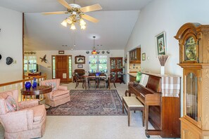 A spacious living room with a piano, a large wooden cabinet, and a dining area with a chandelier. - Peaceful Harrison Home w/ Porch & Grill! (Harrison)