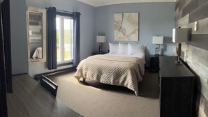 Un dormitorio con cama, dos mesitas de noche con lámparas, un ventanal con cortinas y una obra de arte colgada en la pared.