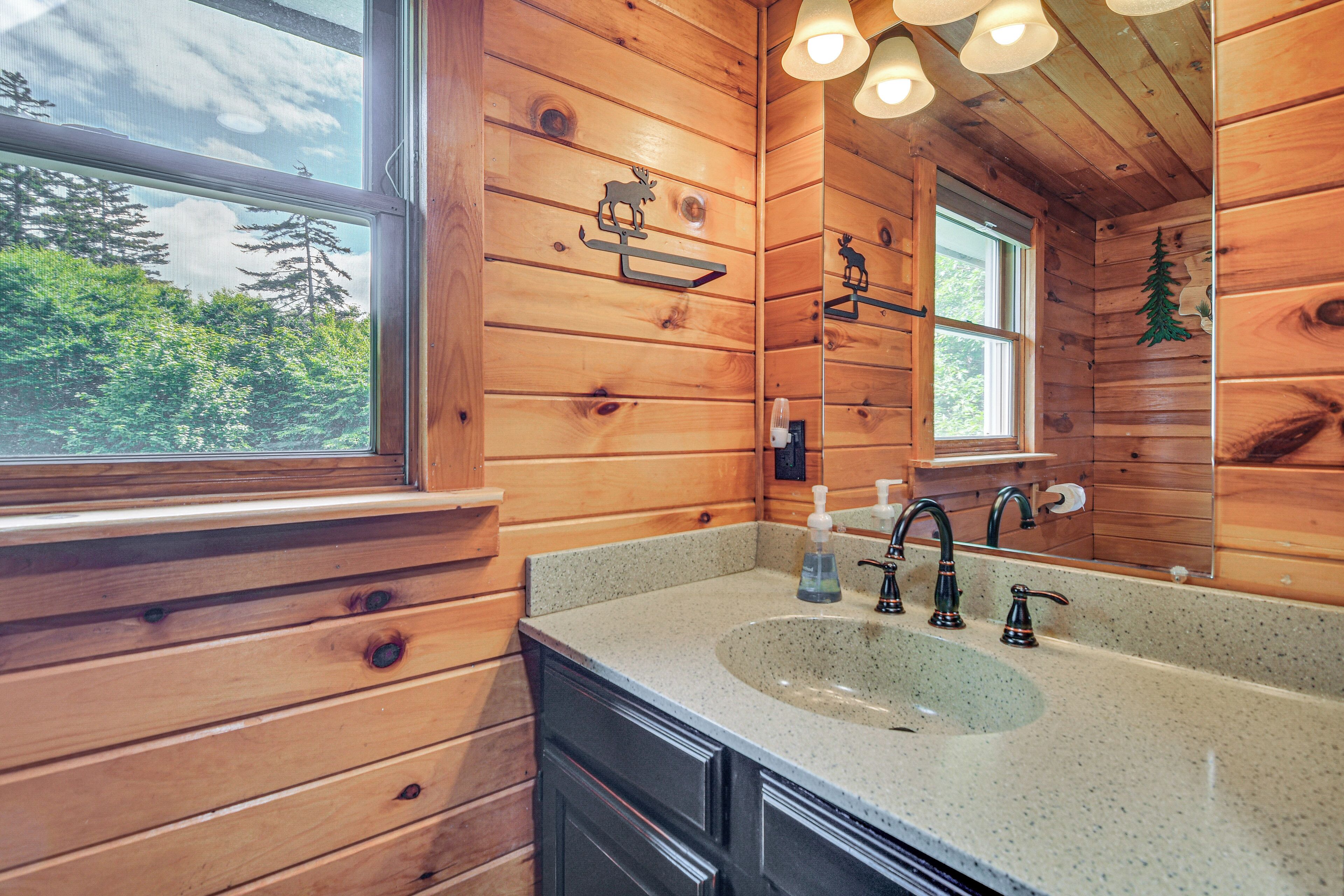 Un bagno in una cabina di legno con un'ampia finestra, un lavandino e uno specchio.