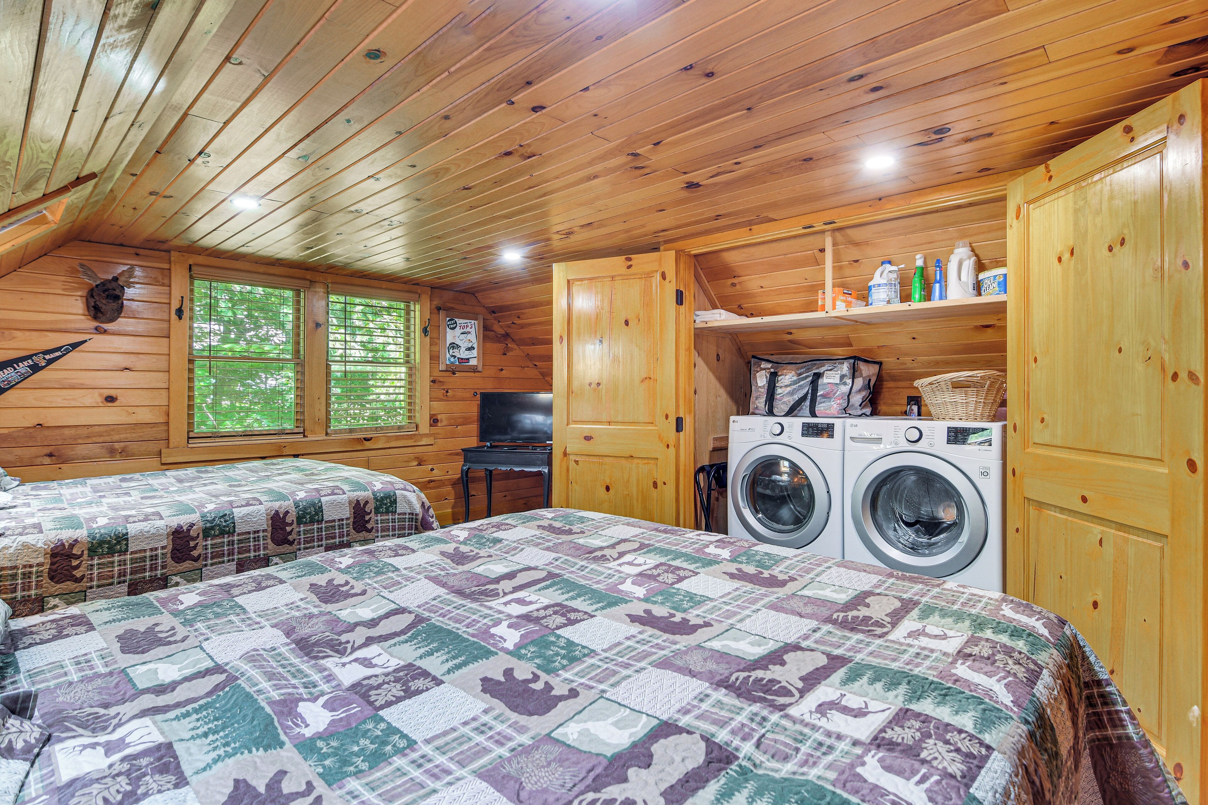Een gezellig vakantiehuisje met houten inrichting, een bed met quilt, een wasmachine en een klein bureau.