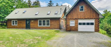 A log cabin with a metal roof, a garage, and a gravel driveway.