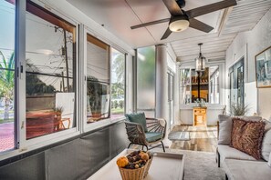 A spacious room with large windows, a ceiling fan, a wicker chair, a sofa, and a small table with a basket. - Bayfront St Petersburg Home w/ Hot Tub & Dock! (St. Petersburg)