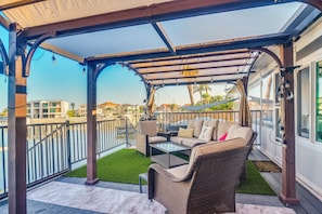 A covered outdoor seating area with wicker furniture, a glass table, and a view of the surrounding buildings and water. - Bayfront St Petersburg Home w/ Hot Tub & Dock! (St. Petersburg)
