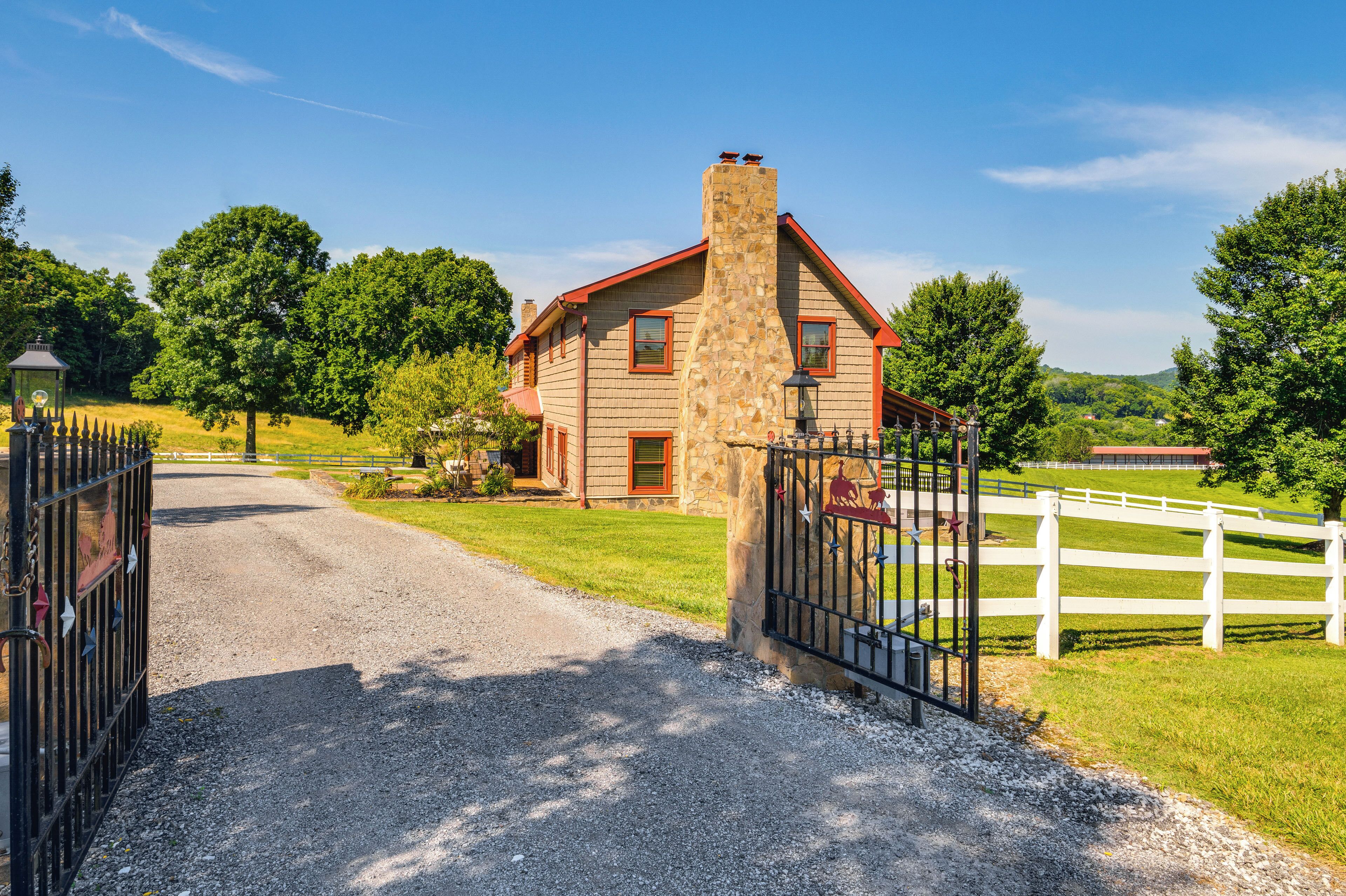 A stone house with a red roof, a gravel driveway, and a white fence.