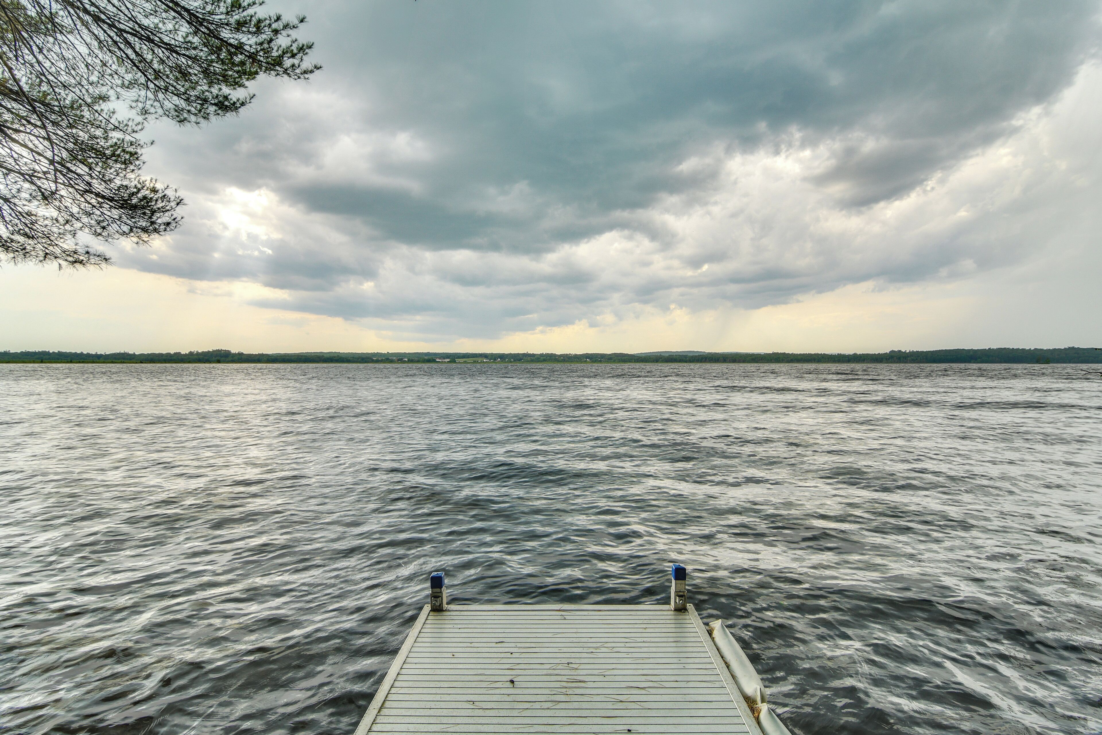 A wooden dock extending into a body of water with a cloudy sky above.