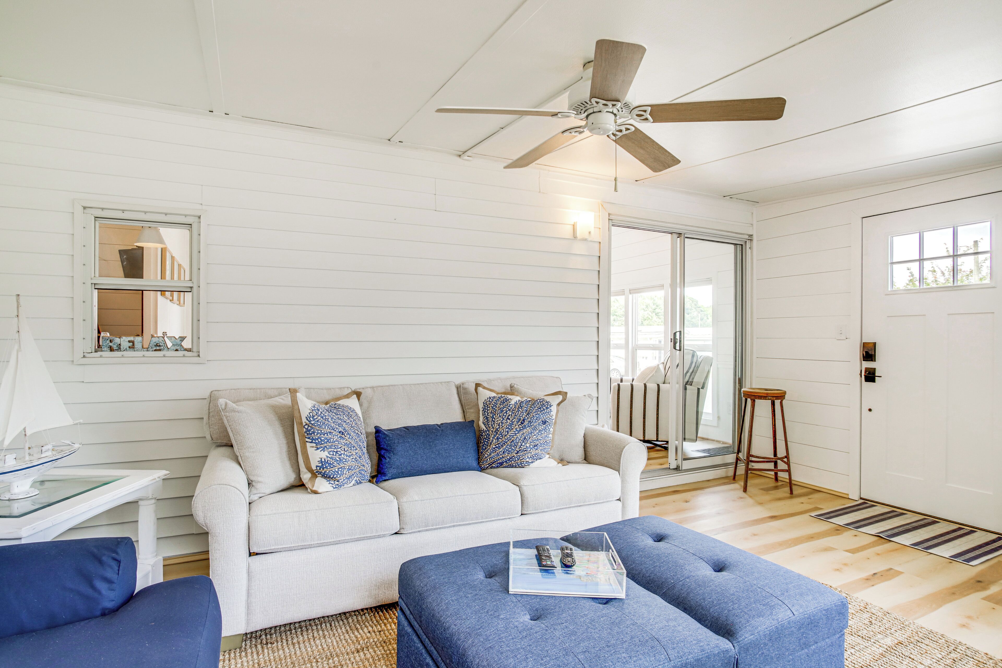 A living room with a white sofa, blue ottoman, and a ceiling fan.