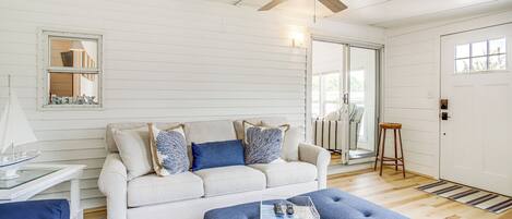 A living room with a white sofa, blue ottoman, and a ceiling fan.
