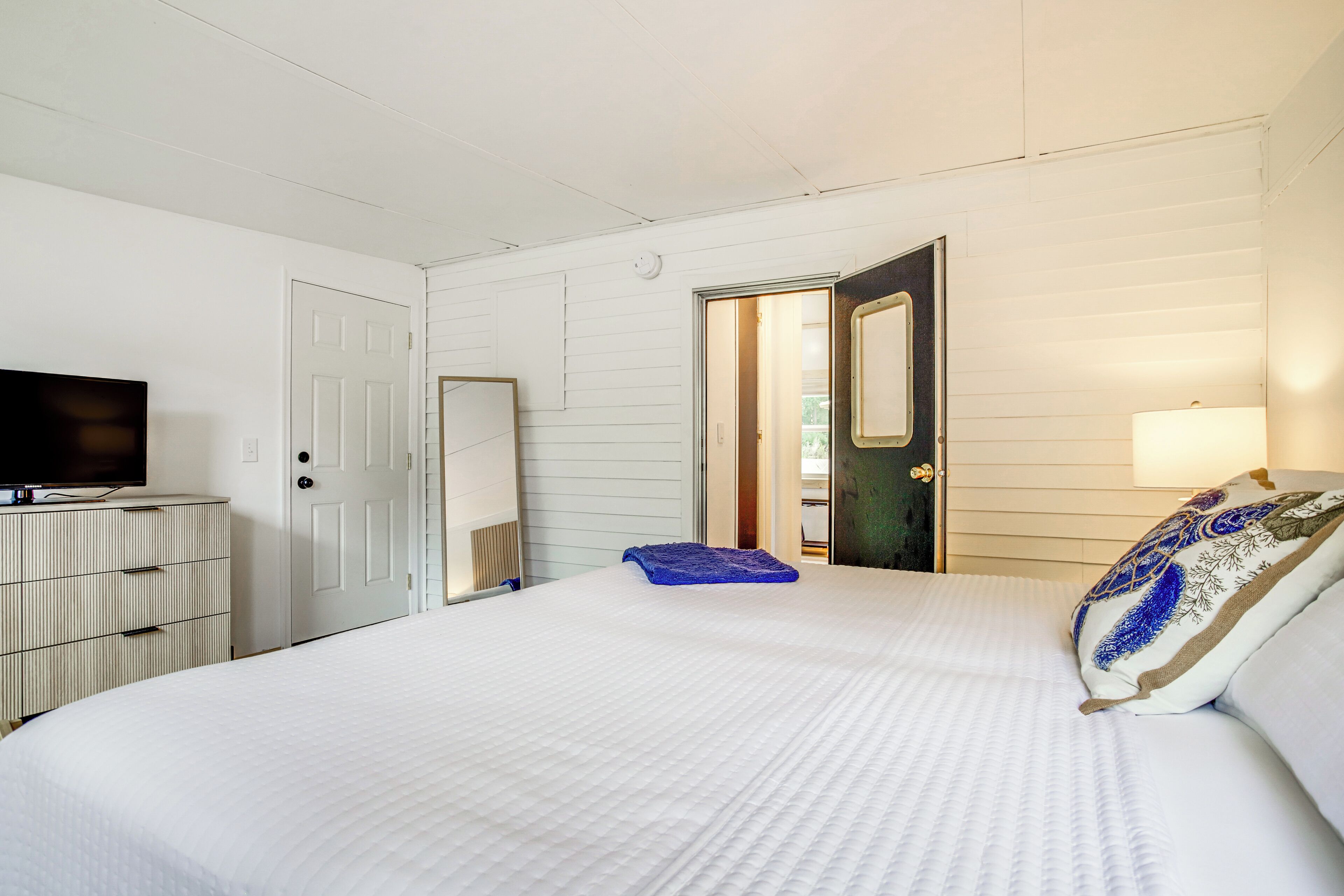 A bedroom with a bed, a dresser, a television, and a door leading to another room.