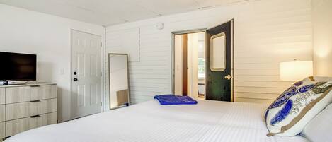A bedroom with a bed, a dresser, a television, and a door leading to another room.