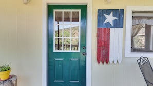 En turkos dörr med ett fönster, en dekoration i form av en Texas-flagga och en krukväxt på ett trästativ.