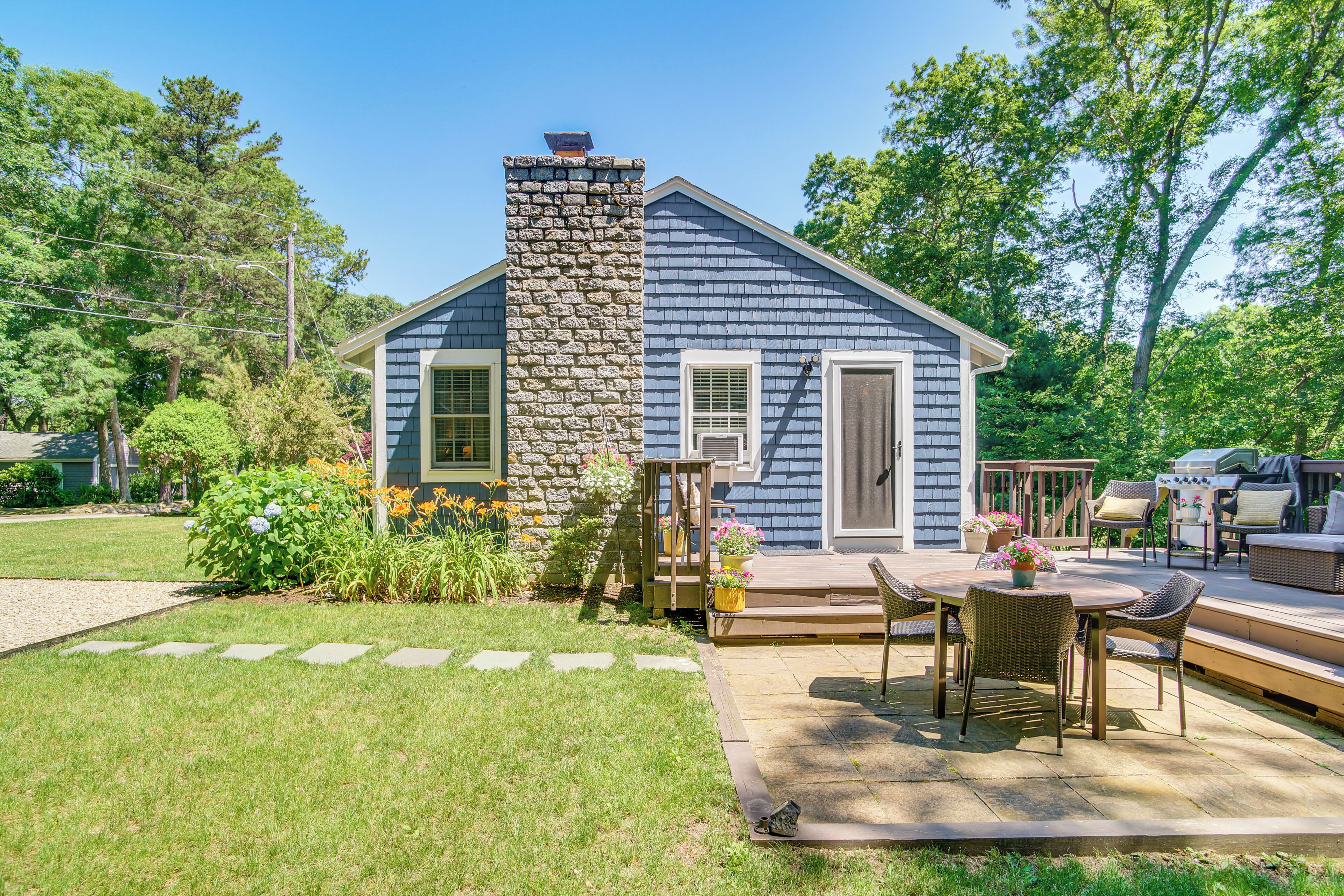 A house with a stone chimney, a deck with outdoor furniture, and a garden with various plants and flowers.