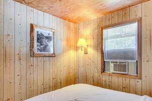 Una habitación con paneles de madera, una cama, un cuadro enmarcado, una lámpara de pared y un equipo de aire acondicionado.