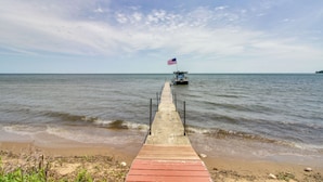 Un muelle de madera que se adentra en aguas tranquilas, con un bote y una bandera estadounidense a lo lejos.