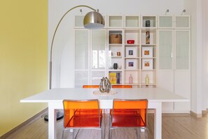 Un comedor con mesa blanca, sillas naranjas y un mueble con puertas de vidrio que contiene varios objetos.