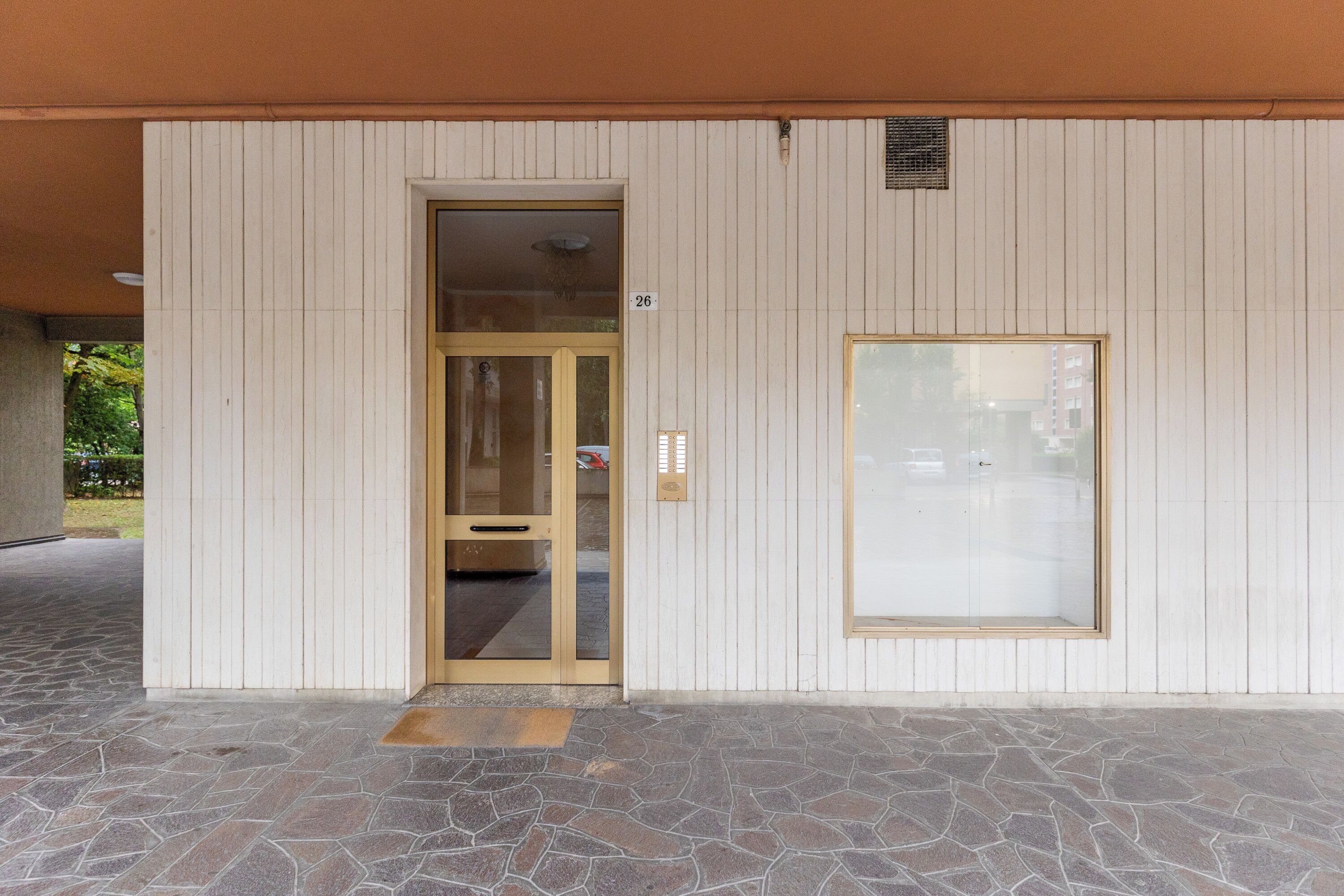 A building entrance with a stone-paved ground, a glass door, and a number sign.