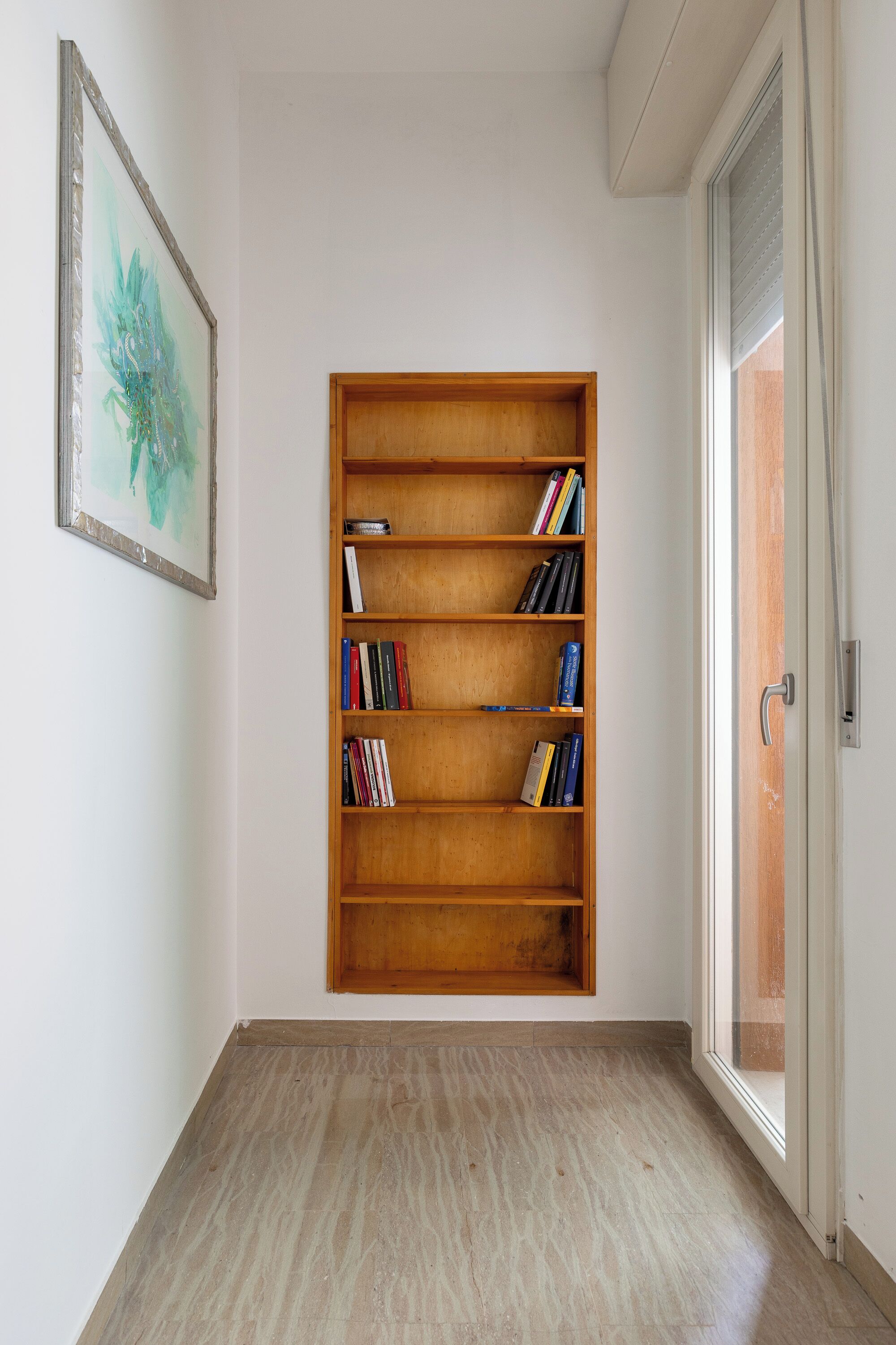 A room with a wooden bookshelf filled with books, a framed picture on the wall, and a sliding glass door.