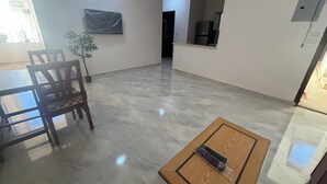 Un salón amplio con suelo de mármol, una mesa de comedor de madera con sillas, una pequeña mesa de centro de madera y una planta en maceta.