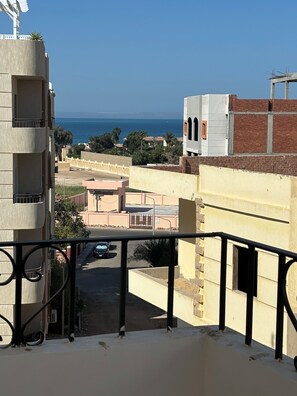 A balcony with a view of the sea, buildings, and a parking area. - Cozy apartment with Seaview from the bedroom (Hurghada)