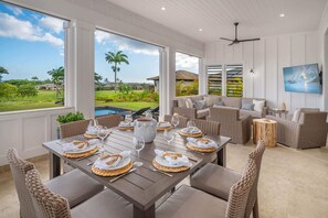 A dining area with a view of a pool and garden, furnished with wicker chairs and a table set for a meal. - Island Villa + Guest House | Pool, Hot Tub, Fire Pit, Hammock & Ocean Views (Koloa)
