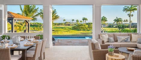 A spacious room with a dining area, a sofa, and a view of a golf course and pool.