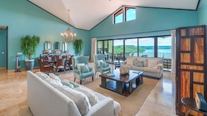 A spacious living room with a high ceiling, large windows, and a view of the outdoors.