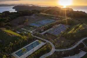 Vista aérea de un resort con múltiples canchas de tenis, una piscina y una vista panorámica del océano.