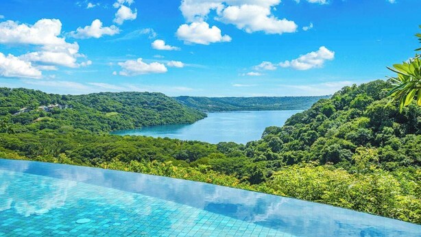 An infinity pool overlooking a lush valley and a lake.